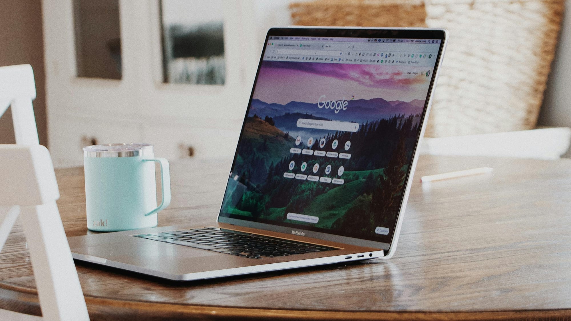 Foto sebuah laptop yang menyala dan sebuah cangkir di atas meja