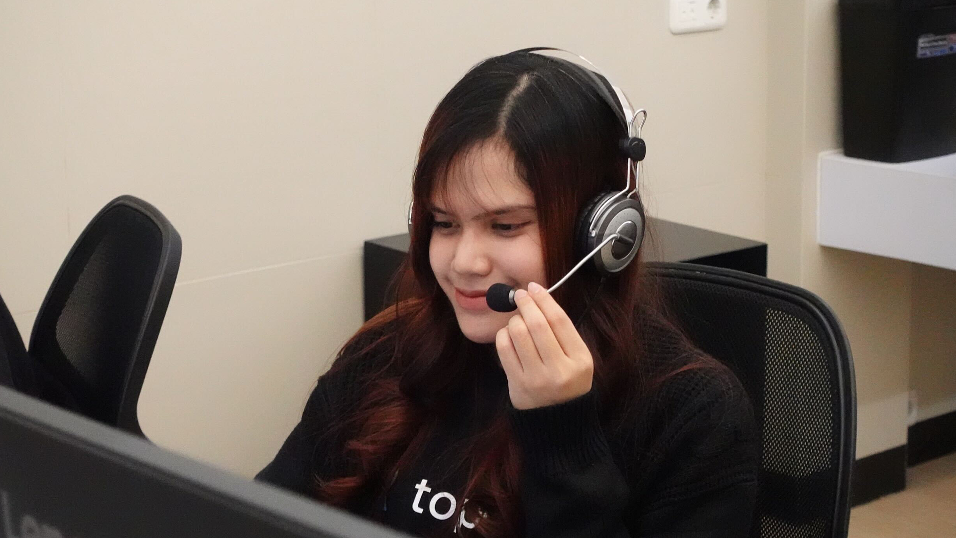 Petugas layanan pelanggan menggunakan headset sedang membantu nasabah terkait layanan keuangan dan remitansi digital di kantor.