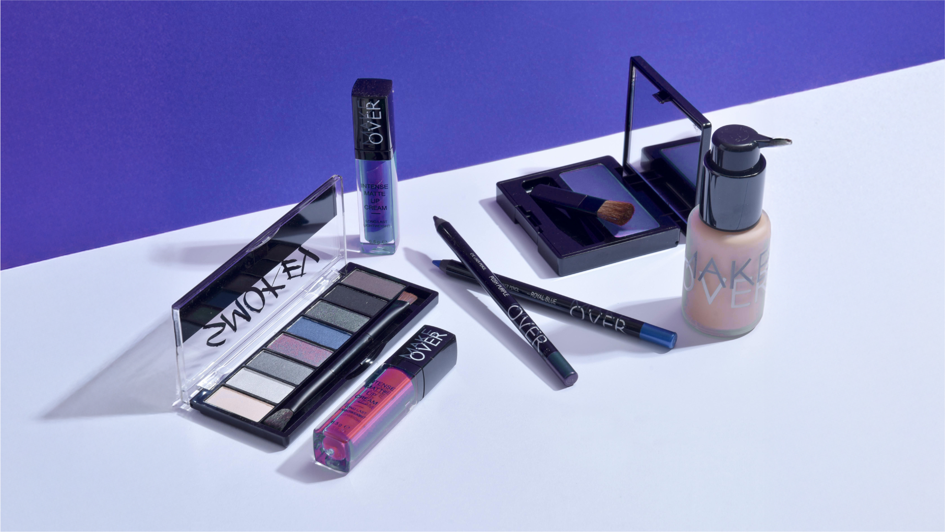 Beberapa produk makeup seperti eyeshadow, lip cream, eyeliner, dan foundation ditata di atas permukaan putih.