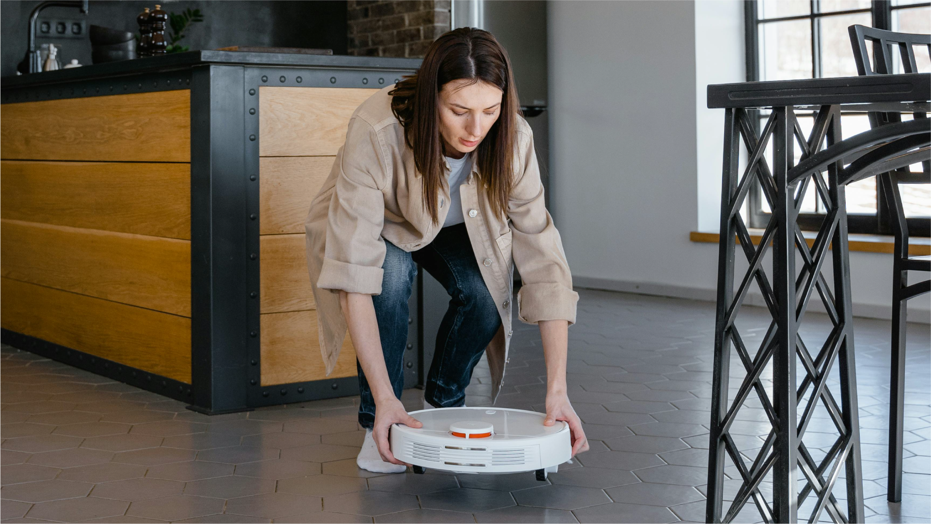 Seorang perempuan sedang meletakkan robot vacuum impor di lantai dalam ruangan rumah modern.