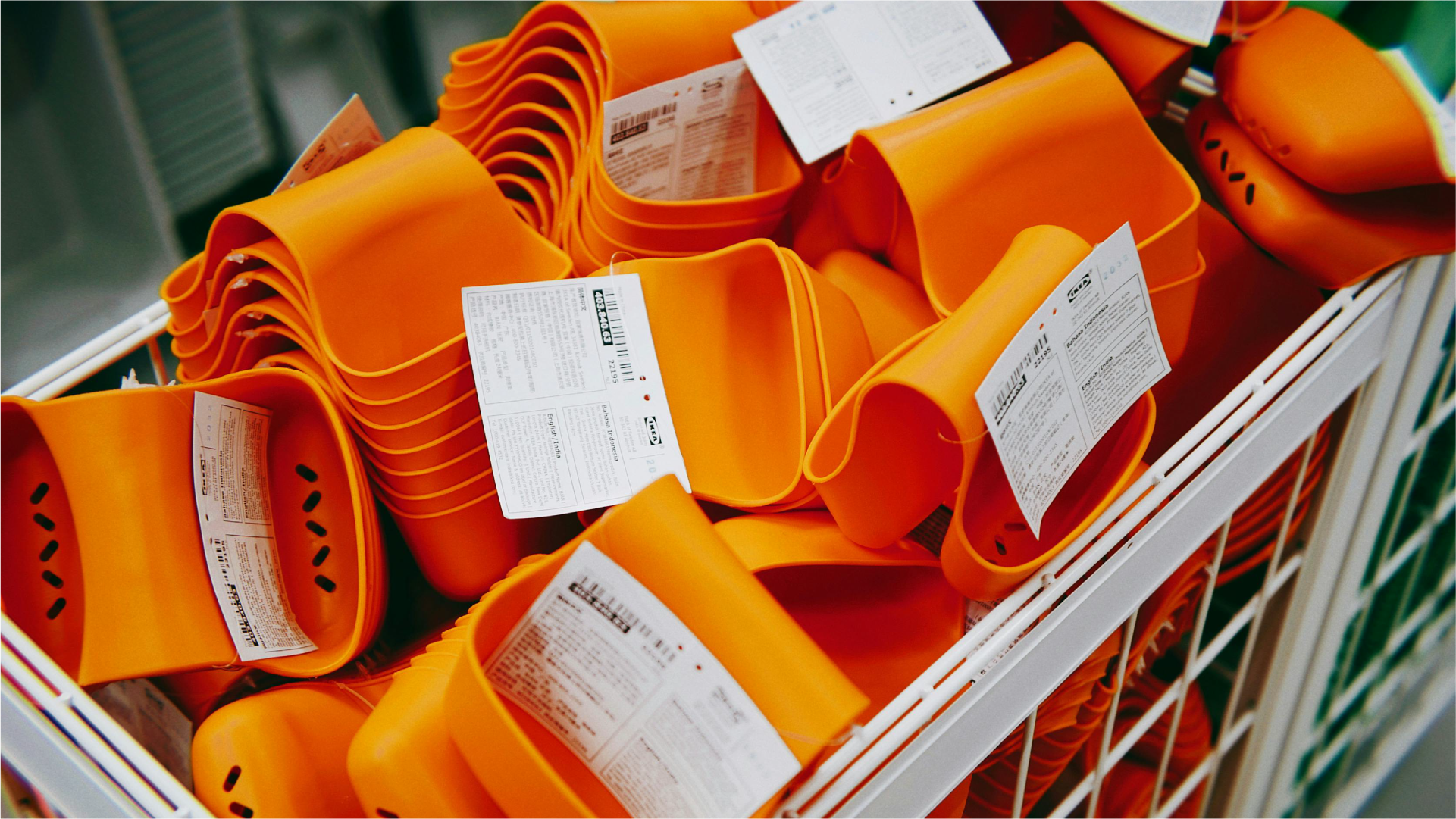 Tumpukan wadah plastik impor berwarna oranye dengan label produk di dalam keranjang toko.