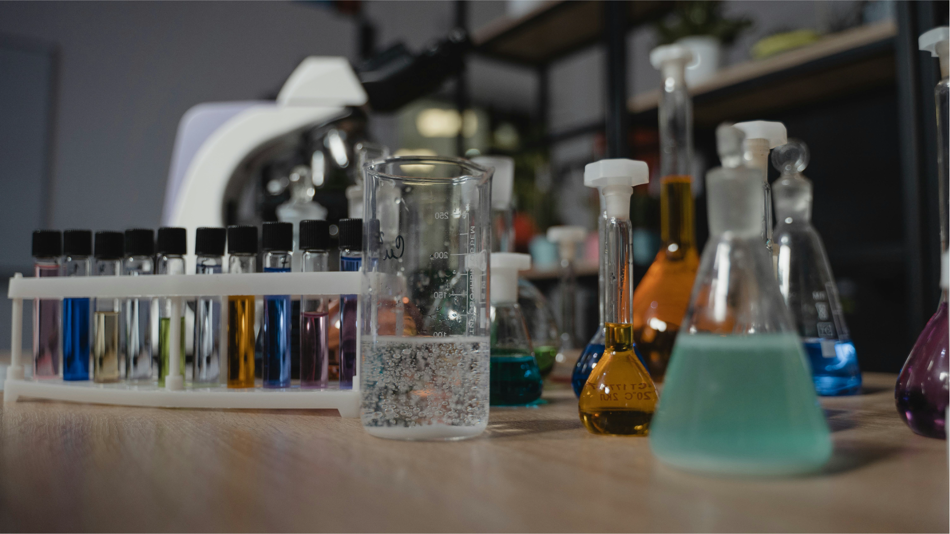 Peralatan laboratorium seperti tabung reaksi, gelas ukur, dan labu berisi cairan warna-warni di atas meja.