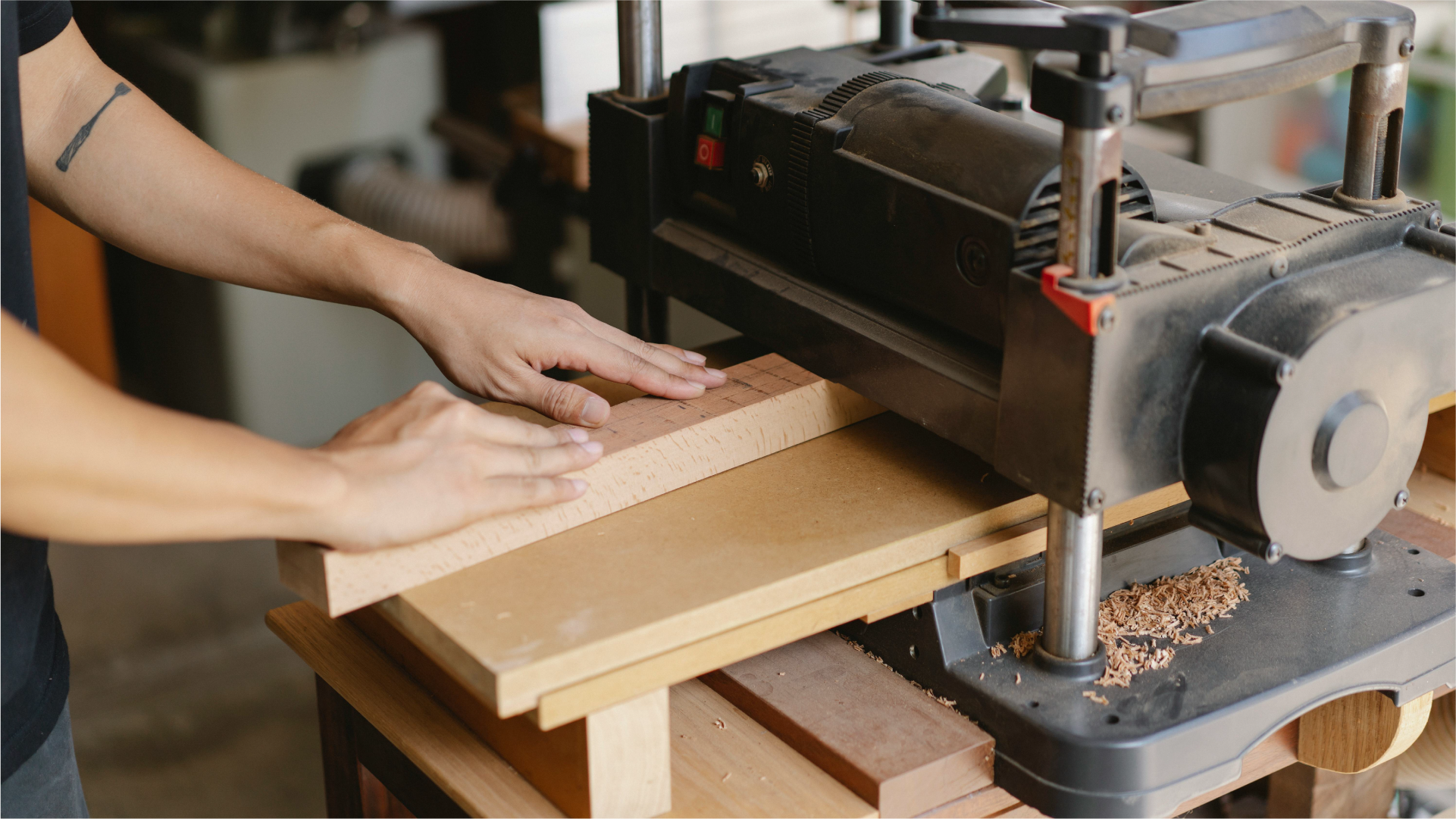 Seseorang mengoperasikan mesin planer impor untuk meratakan permukaan papan kayu di workshop.