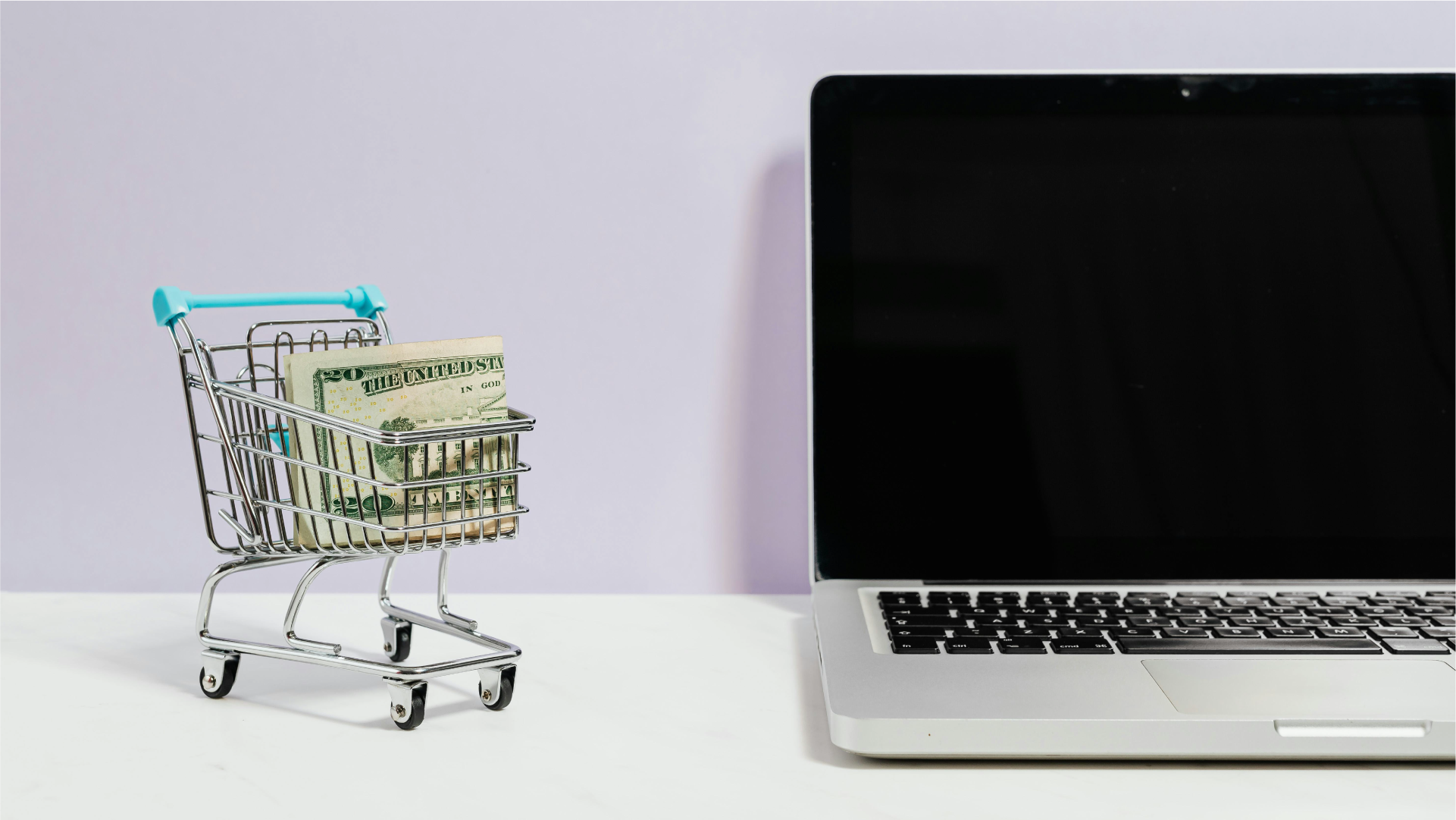 Keranjang belanja kecil berisi uang USD di samping laptop, menggambarkan pembayaran supplier luar negeri secara online.