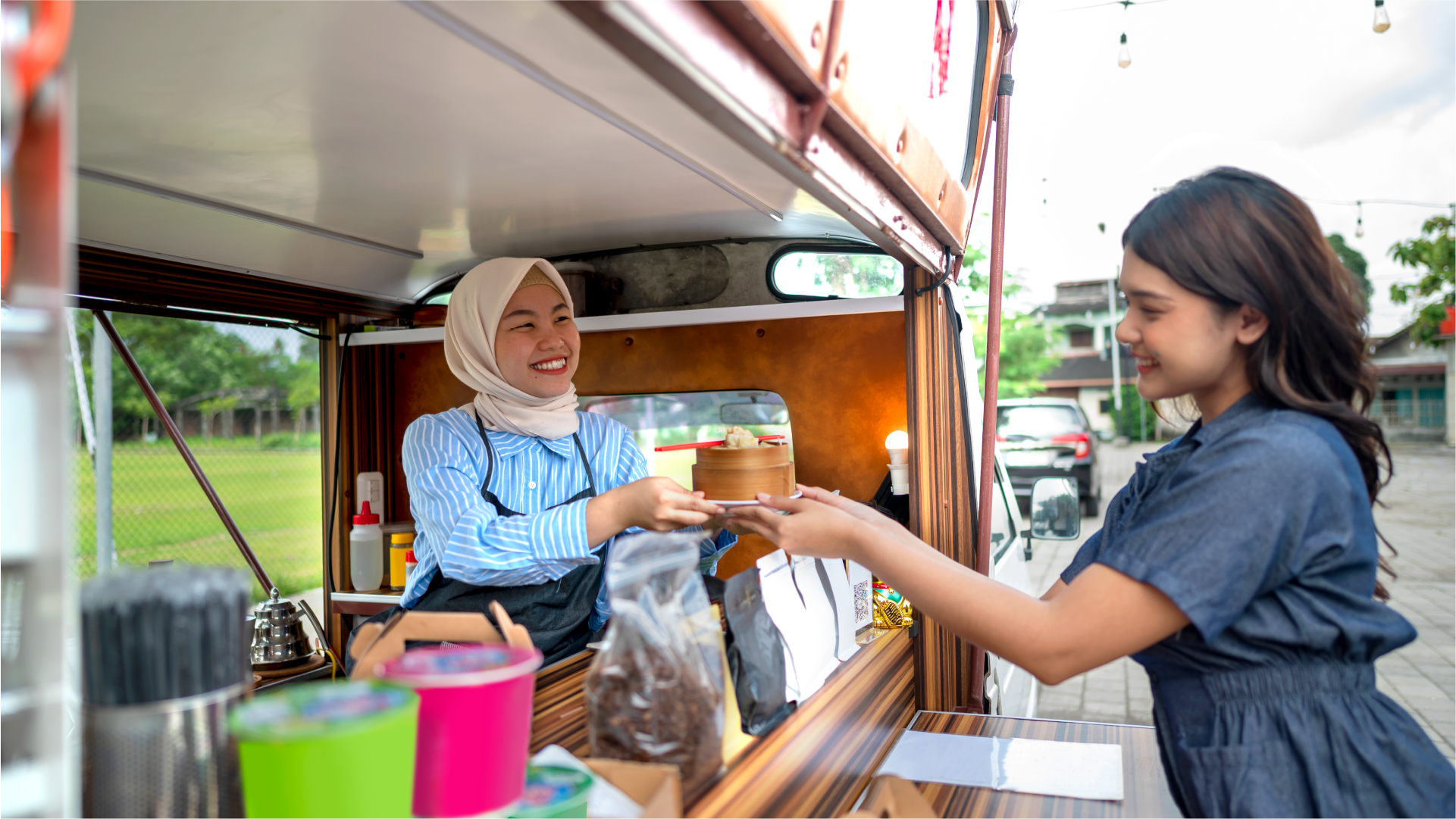Pelaku usaha mikro menyerahkan pesanan kepada pelanggan di kios makanan, menggambarkan aktivitas ekonomi lokal dan peran remitansi dalam mendukung usaha kecil.