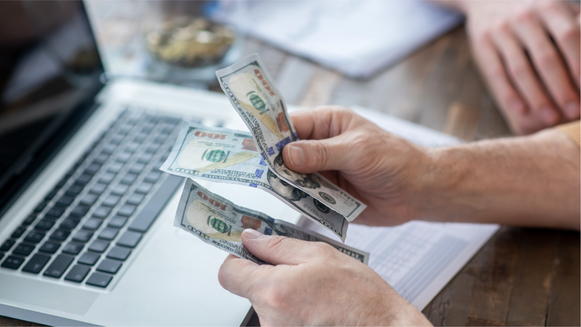 Seseorang menghitung uang dolar di dekat laptop untuk mengecek dana transaksi dari luar negeri.