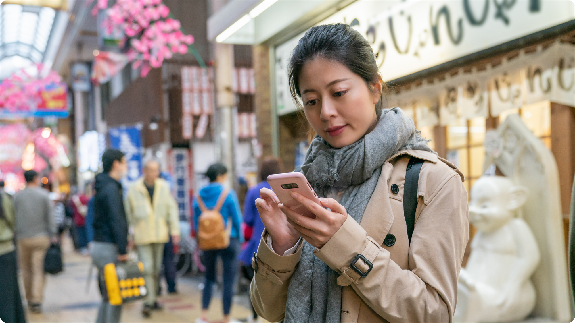 eorang pengguna membuka smartphone di kawasan komersial Jepang sebagai ilustrasi kemudahan kirim uang ke Jepang secara online.