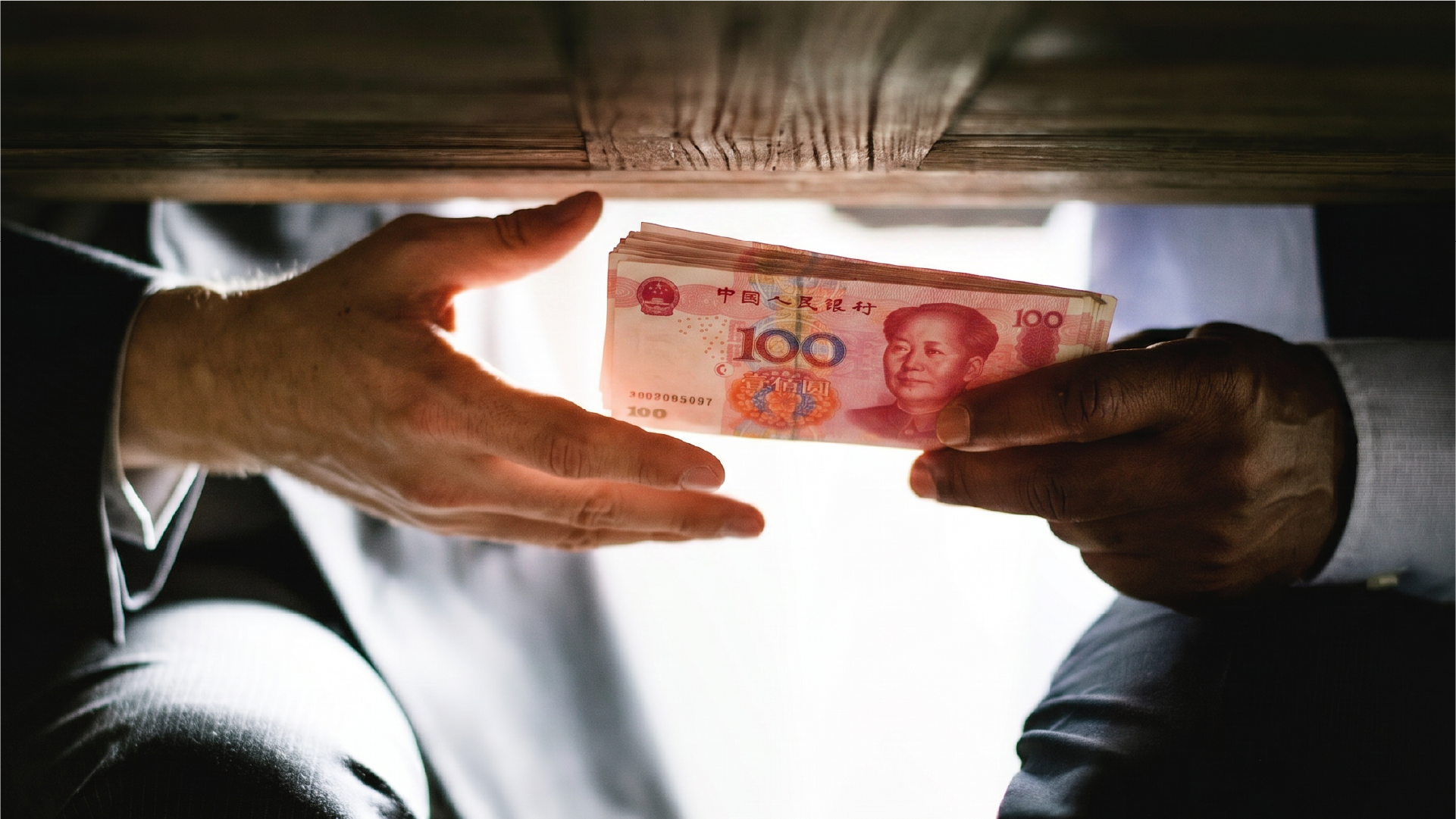 桌下进行人民币现金交易，象征地下钱庄和非正规汇款渠道的风险