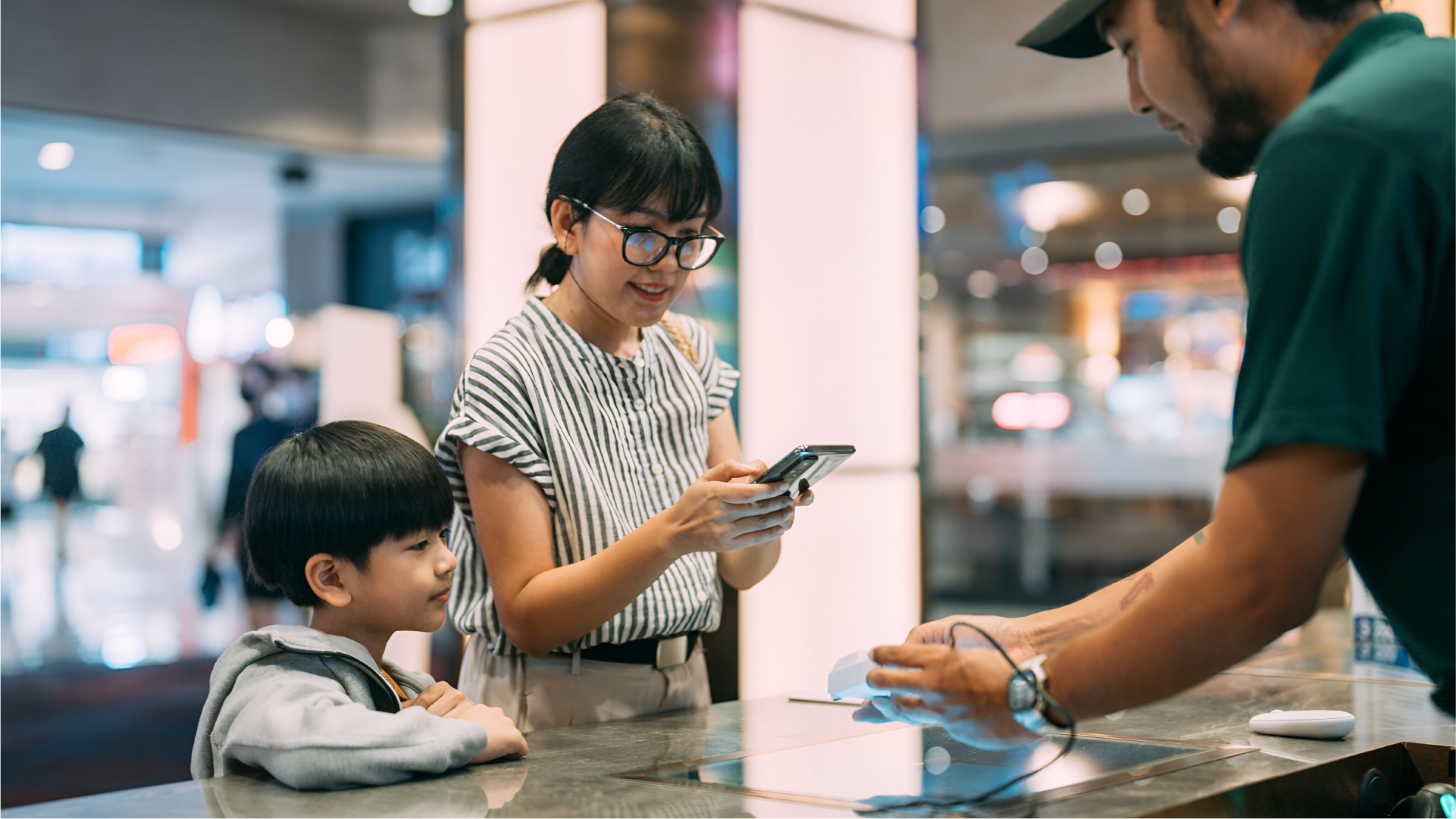 Seorang pengguna memegang smartphone saat melakukan pembayaran digital di meja kasir bersama anaknya.