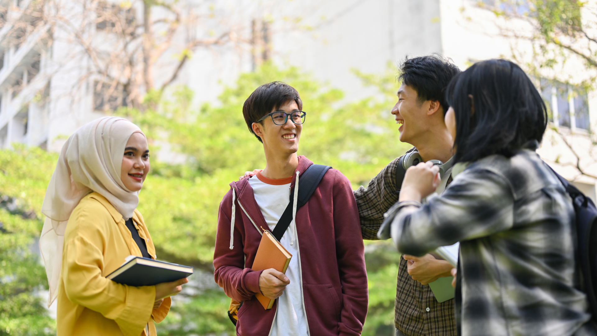 Sekelompok mahasiswa berbincang di area kampus sambil membawa buku untuk perkuliahan