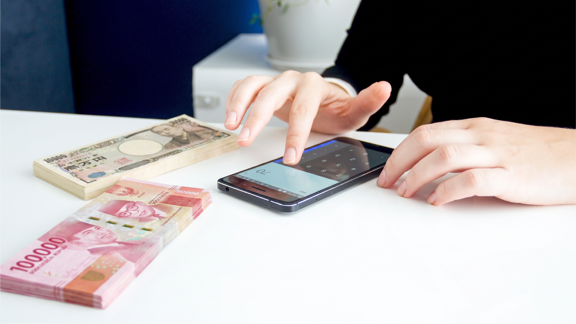 ルピアと日本円の紙幣を横に、スマホの電卓で金額を計算する様子