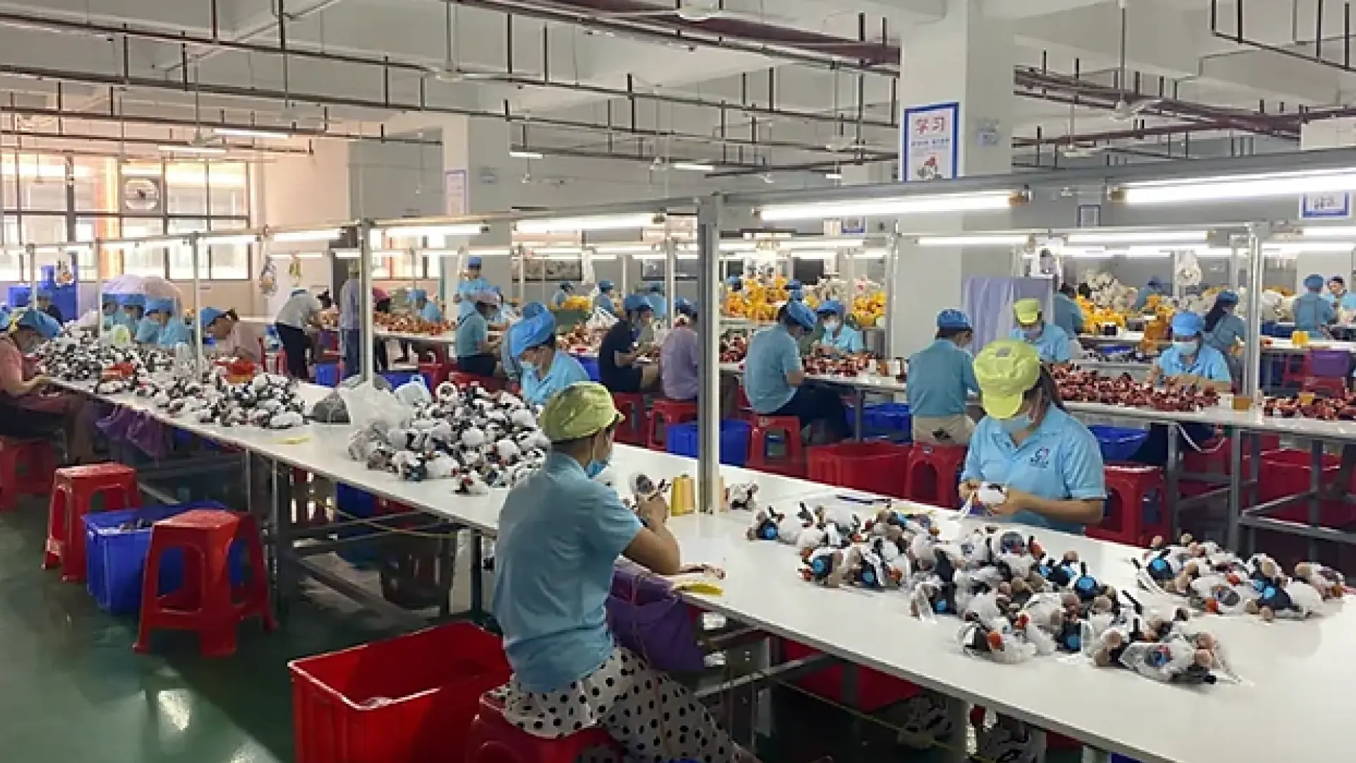 Para pekerja merakit produk mainan di lini produksi pabrik dengan berbagai komponen mainan di atas meja.