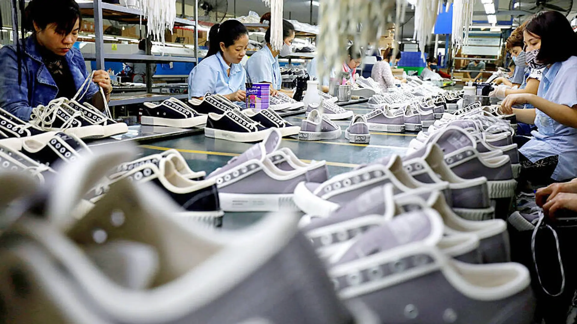 Para pekerja merakit sepatu di pabrik alas kaki dengan deretan sepatu pada lini produksi.