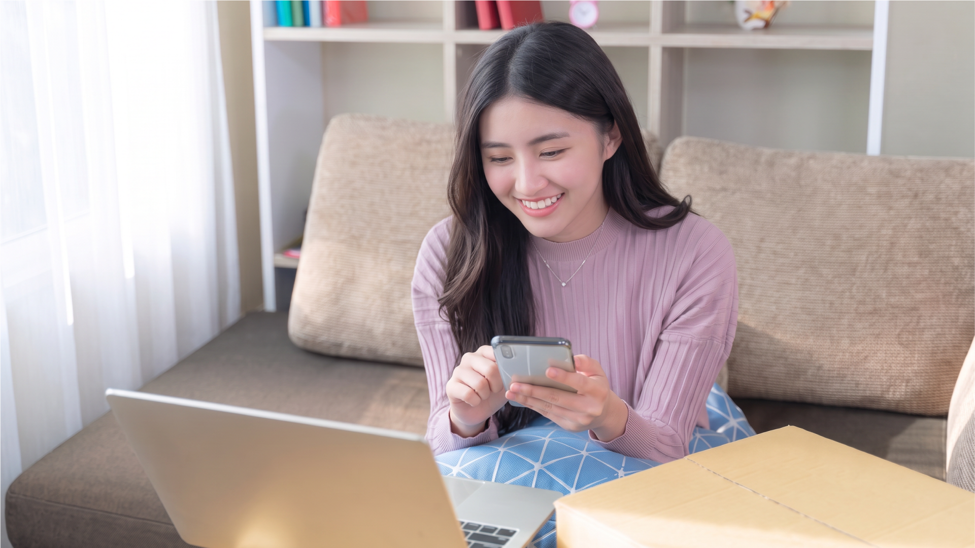 Perempuan menggunakan smartphone dan laptop untuk melakukan transfer uang internasional secara online