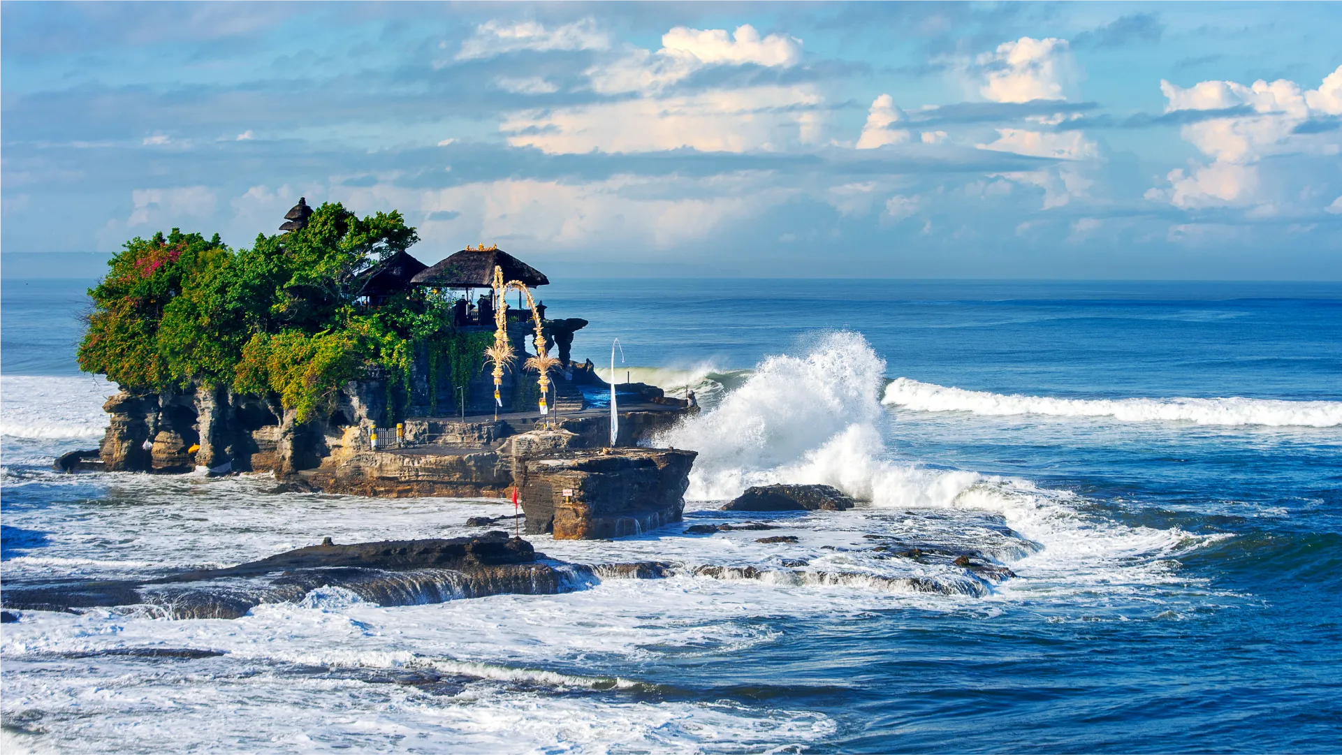 位于 Bali 的 Tanah Lot 寺庙建在海边的岩石上,四周海浪拍打,远处是蓝天。