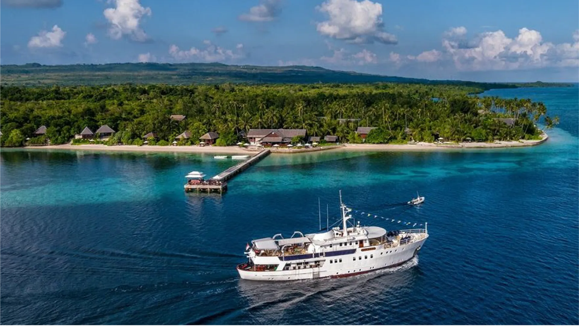 Wakatobi 的清澈蓝色海域中停着一艘游船,附近的热带小岛上有栈桥和海滨住宿设施。