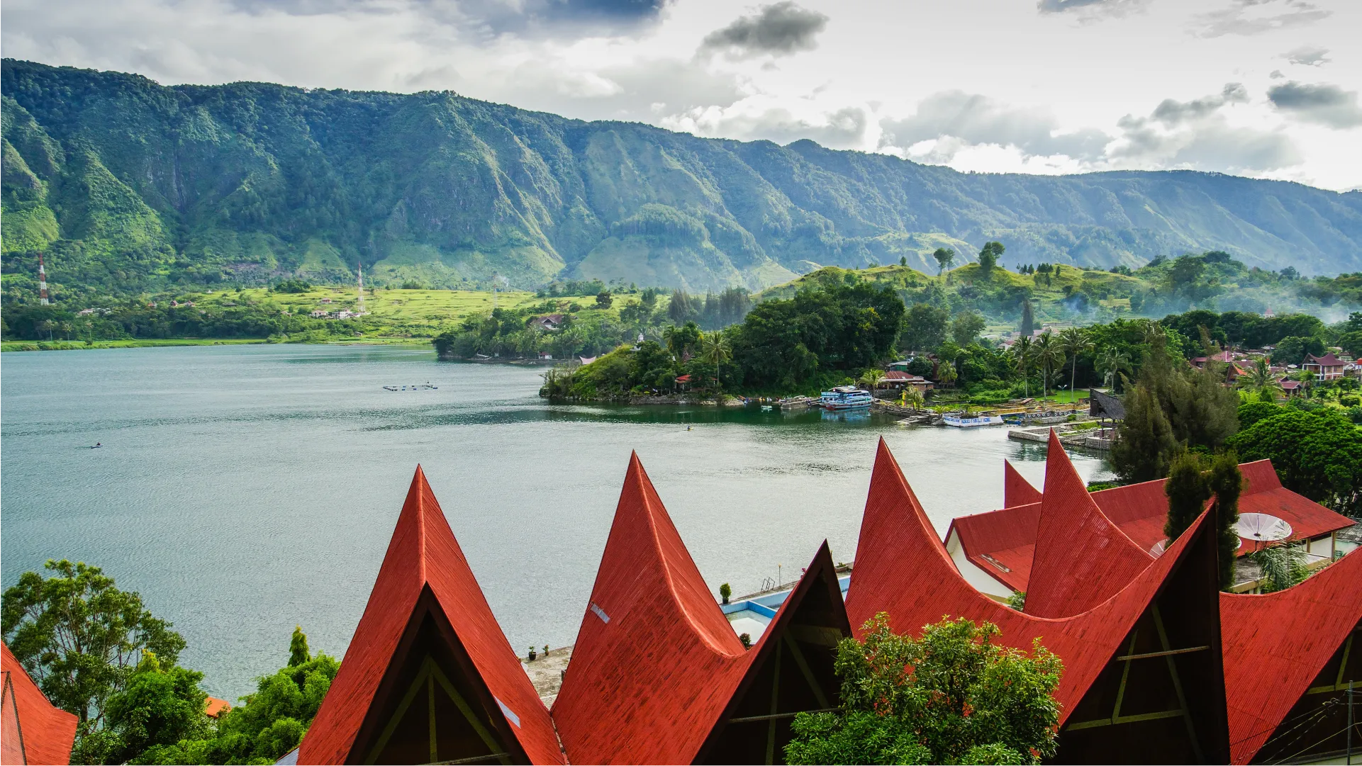 Sumatera Utara 的 Danau Toba 湖景,前景是具有特色屋顶的 Batak 传统房屋,周围环绕着绿色山丘。