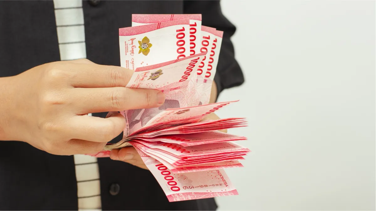 Seseorang sedang menghitung lembaran uang IDR 100,000 untuk kirim uang ke luar negeri.