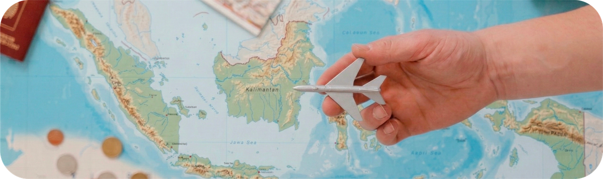 Hand holding a small airplane model above a map of Indonesia during travel planning.