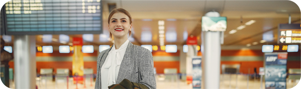 Ekspatriat wanita di bandara dengan informasi jadwal penerbangan sebagai simbol mobilitas kerja internasional.