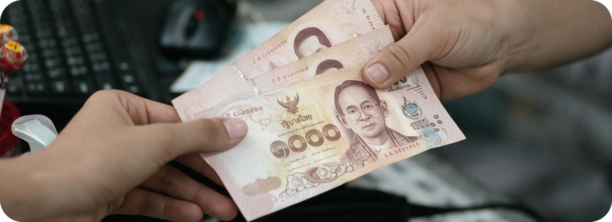 Proses penyerahan uang tunai Baht Thailand sebagai ilustrasi kirim uang ke Thailand dari Indonesia