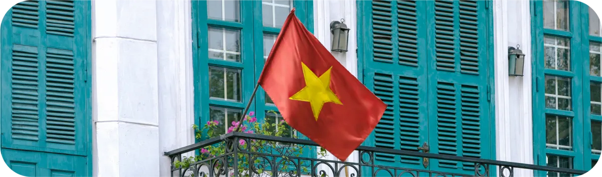 Bendera Vietnam berwarna merah dengan bintang kuning terpasang di balkon bangunan dengan jendela hijau.