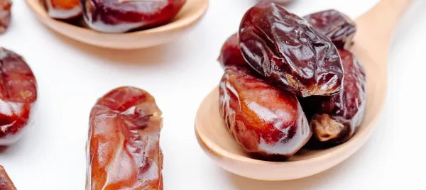Beberapa buah kurma berwarna kecokelatan di atas sebuah sendok kayu