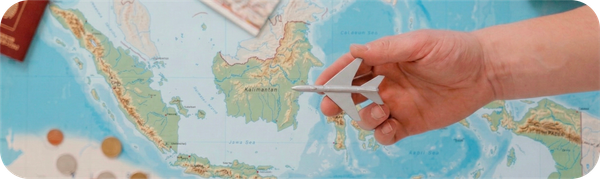 Hand holding a small airplane model above a map of Indonesia during travel planning.