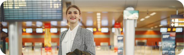 Ekspatriat wanita di bandara dengan informasi jadwal penerbangan sebagai simbol mobilitas kerja internasional.