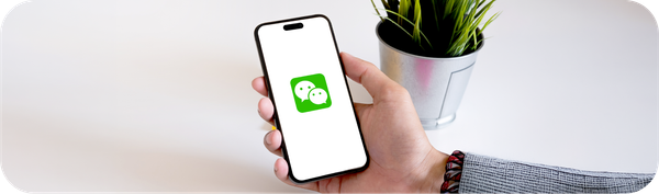 Tangan memegang smartphone dengan logo WeChat sebagai ilustrasi layanan pembayaran digital WeChat Pay.