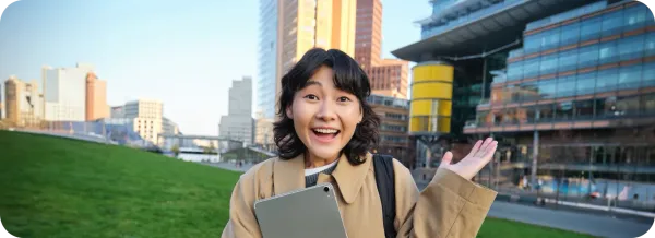 Mahasiswi Asia memegang tablet dengan latar kawasan kampus modern sebagai ilustrasi kuliah di universitas terbaik Jepang.