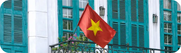 Bendera Vietnam berwarna merah dengan bintang kuning terpasang di balkon bangunan dengan jendela hijau.